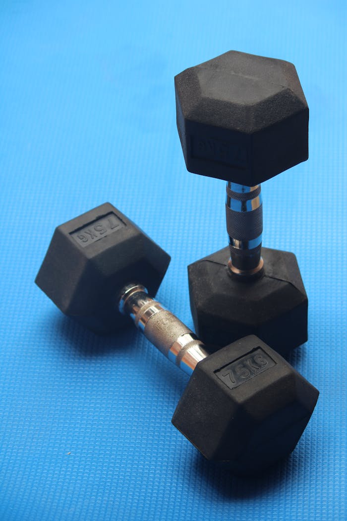 services-03 Three steel dumbbells resting on a blue exercise mat, ideal for gym and fitness concepts.
