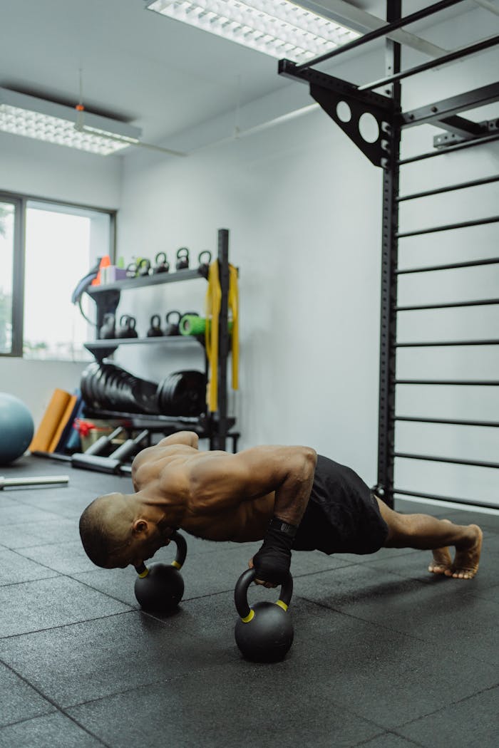services-04 Athletic man doing push-ups on kettlebells in a modern gym setting.