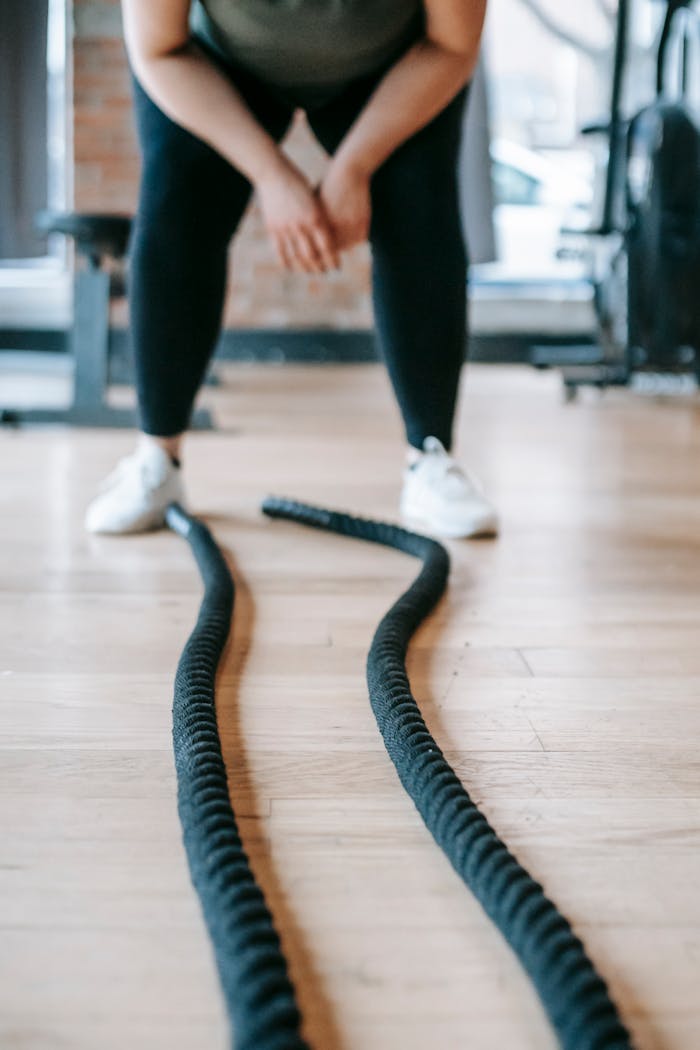 Crop unrecognizable female in activewear near battle ropes during training in gym with sports equipment