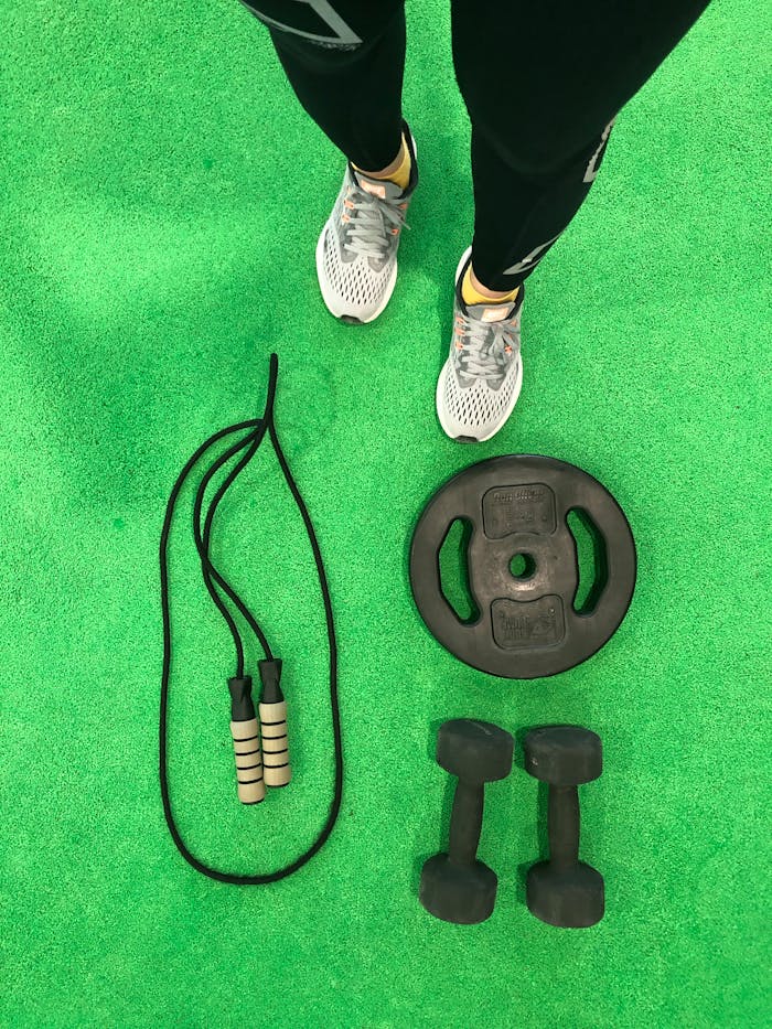 hero-img Flat lay of dumbbells, weight plate, and skipping rope on a green gym floor.